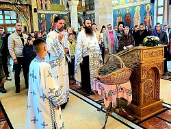 Детаљан кадар чина освећења врбице унутар златиборског храма Преображења. Свештеник Милан Н. са кадионицом у руци кади снопове врбових гранчица положених на украшено дрвено постоље испред олтарске преграде. Дим тамјана се издиже према куполи, додајући мистичност сцени. Верни народ, међу којима су и становници Чајетине и туристи, стоји са упаљеним свећама, пажљиво пратећи молитвени обред. Иконостас у позадини, са својим топлим дрвеним тоновима, чини савршен контраст златним одеждама свештенства. Фотографија је кључна за приказ богослужбеног живота на Златибору током Васкршњег поста 2026. године.